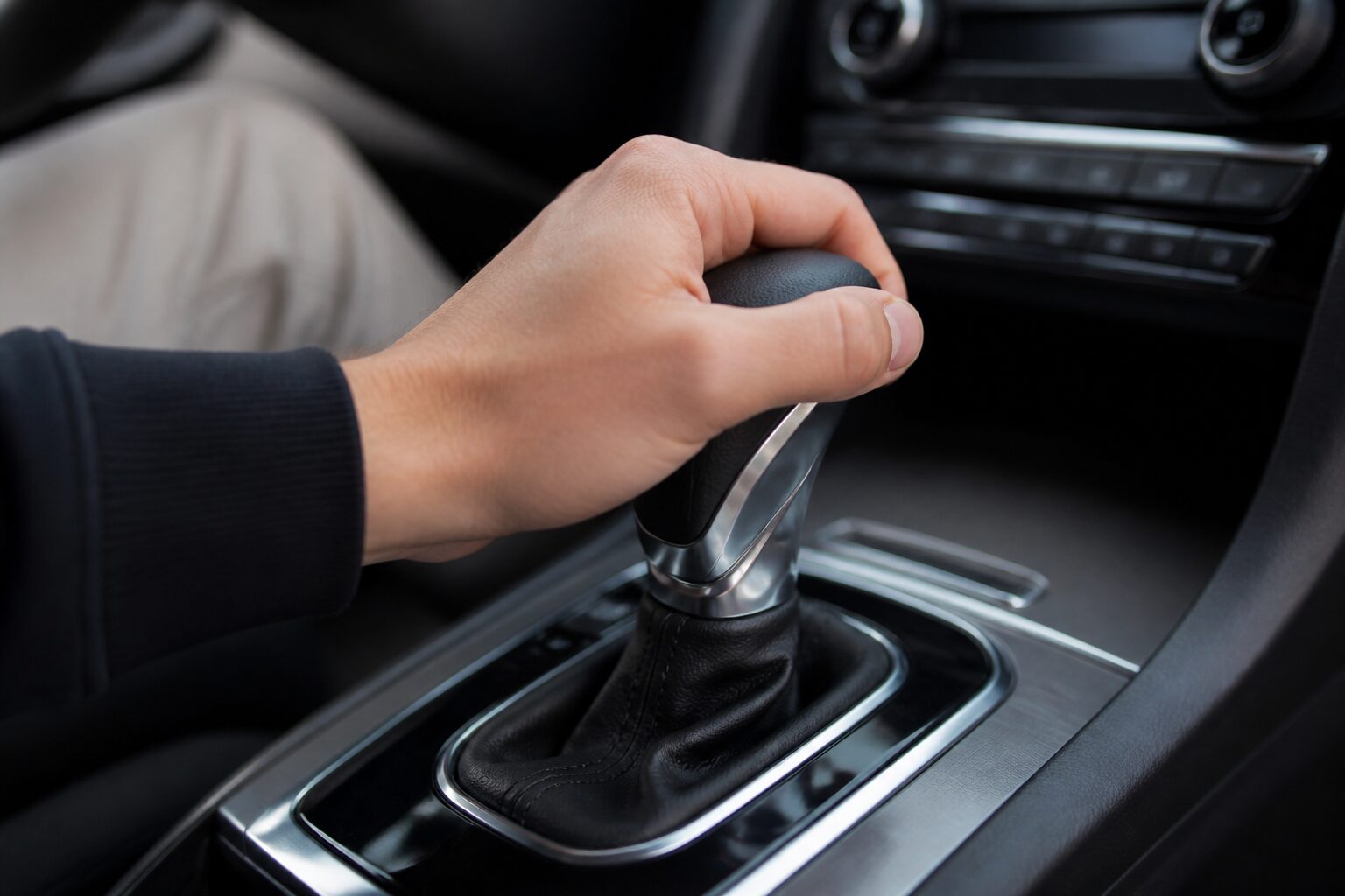 Mão do motorista segurando a alavanca do câmbio automático em um interior de carro moderno, em close e com iluminação suave.