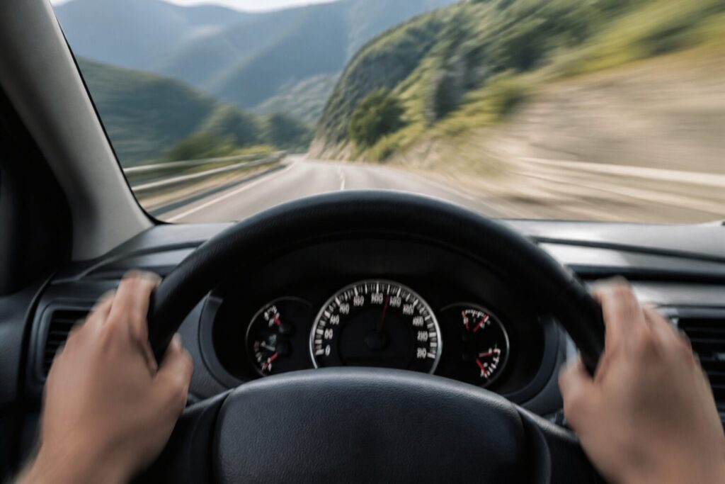 Mãos no volante com leve desfoque de vibração e velocímetro marcando alta velocidade dentro do carro.