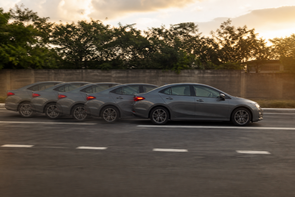 Carro freando em pista seca com marcas de frenagem e marcações de distância no asfalto, visto de lado em movimento.